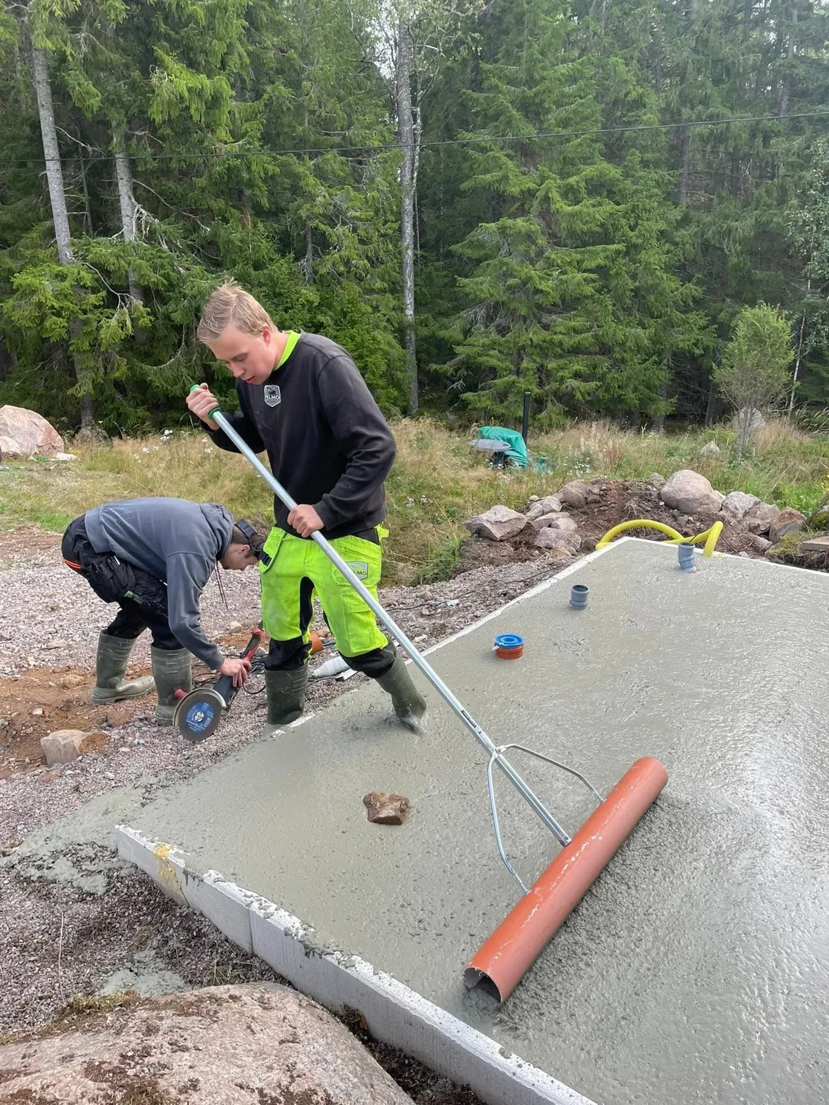 Två personer gjuter en betongplatta, en jämnar till och en kapar