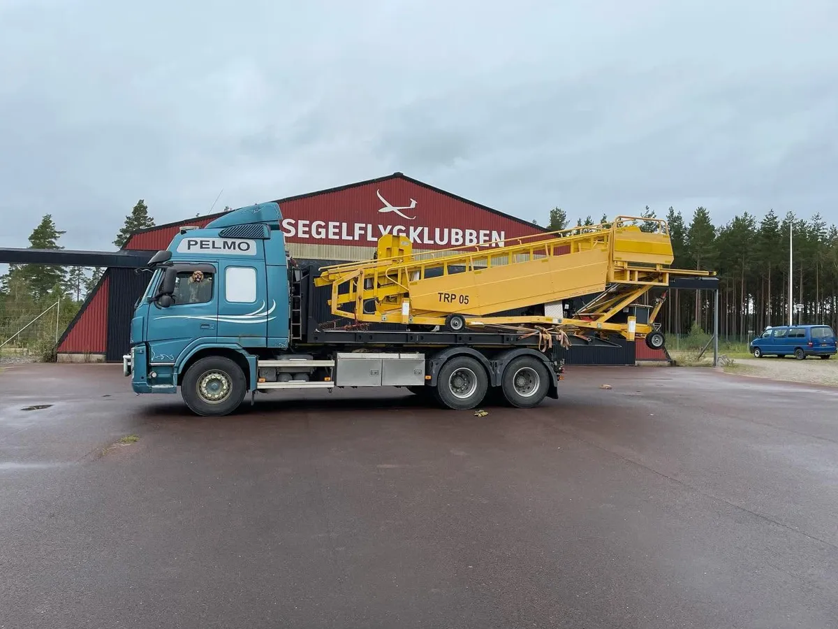 Blå lastbil med en gul maskin fastspänd på flaket