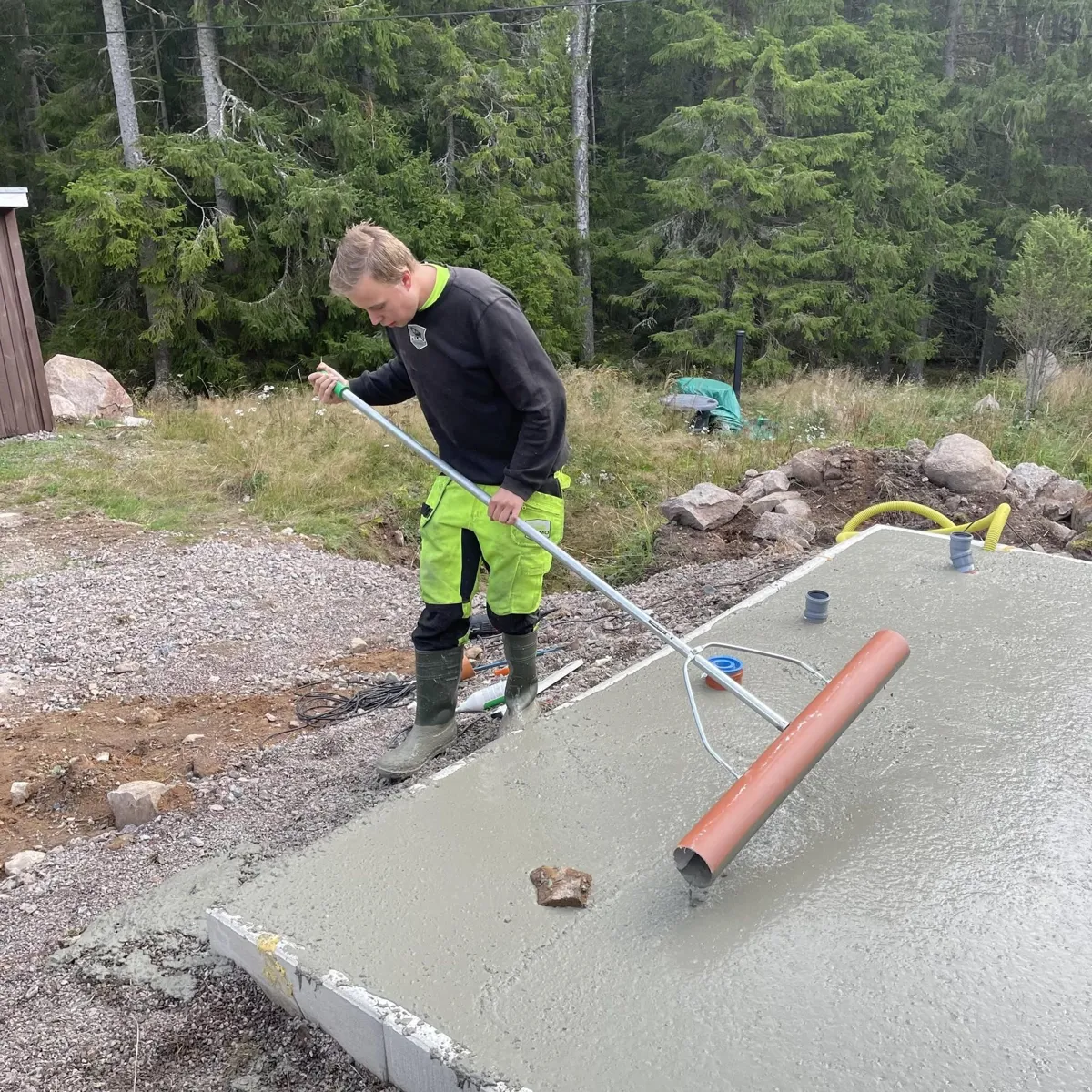 Pelle jämnar till en nygjuten betongplatta vid skogskanten